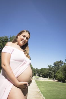 Seven month pregnant woman standing dressed in pink. Happy expression