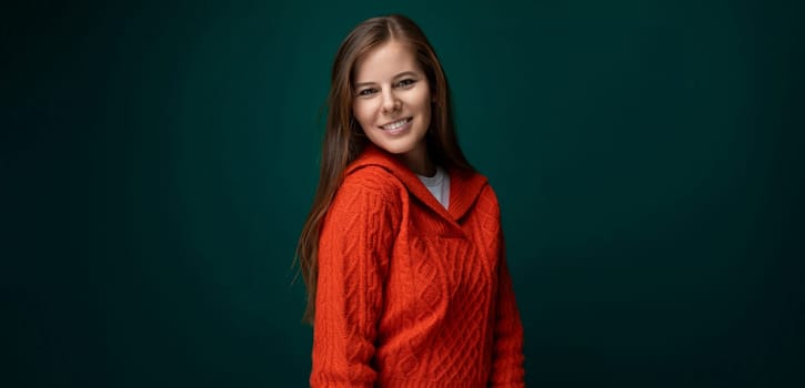 Charming young woman with brown straight hair dressed in a red sweater on a green background with copy space.