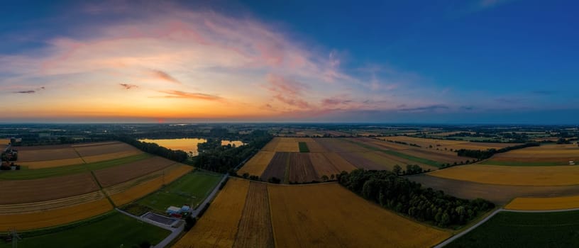 Aerial view capturing the tranquil beauty of vast farmlands at sunset, with the horizon painted in hues of orange and blue