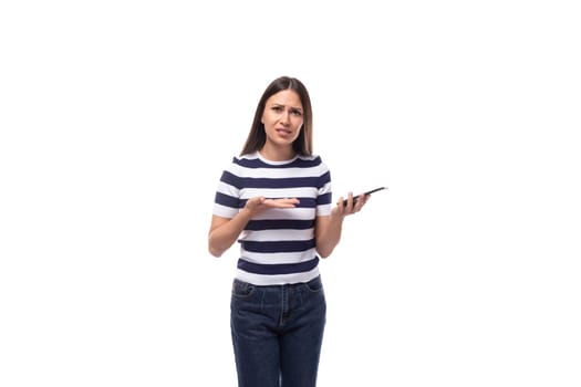 young slender european woman with black straight hair dressed in a striped black and white t-shirt doubts holding a phone.