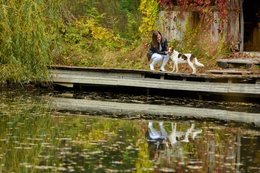Young beautiful girl petting a dog near a lake in an autumn park a