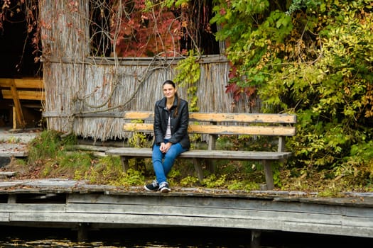 A young beautiful girl in casual clothes sits on a bench in an autumn park a