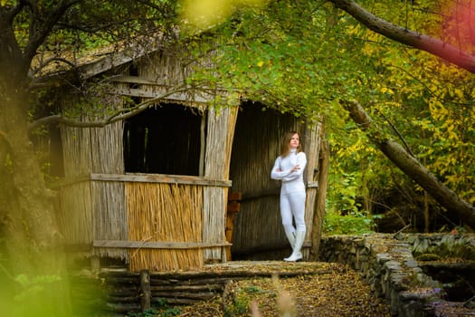 A young beautiful girl in white clothes stands near an old abandoned house in the forest a