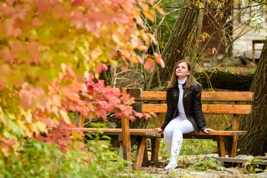 A young beautiful girl sits on a bench and enjoys the autumn landscape a