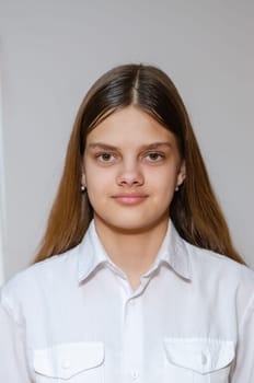 Portrait of a fourteen-year-old girl in a white shirt on a gray background a