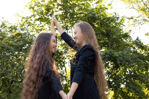 Siblings Day Two Children, Sisters Smile Holding Hands, Looking At Each Other, Green Trees, Park on Background. Love. Joyful Carefree Girls Lifestyle Childhood. Horizontal. Brothers and Sisters Day