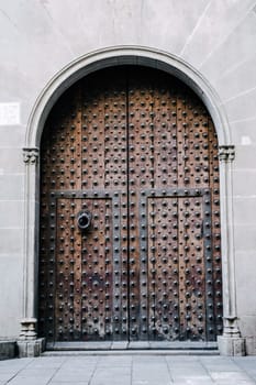 A medieval closed door with iron fittings in a stone wall. Typical architecture of Europe. Ornate medieval doorway in Barcelona Catalonia. High quality picture for wallpaper, article