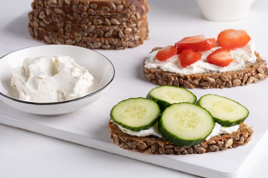 Rye bread with cream cheese and cucumbers, strawberry on a white table. Whole grain rye bread with seeds.