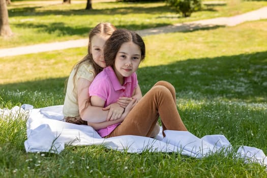 Siblings Day Two Children, Sisters Sit on Grass Hugging. Green Trees, Park on Background. Love. Joyful Carefree Girls Lifestyle Childhood. Horizontal. Brothers and Sisters Day. Horizontal Plane