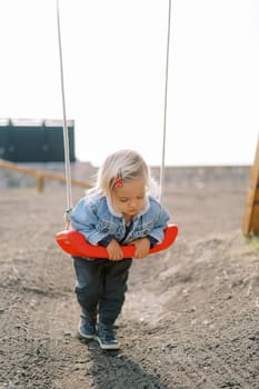 Little girl lies on her stomach on a swing, holding on to it with her hands. High quality photo