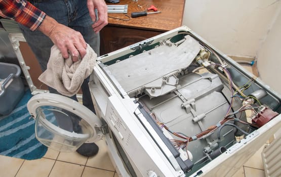 a male handyman removed the lid of the washing machine and wiped the dust inside with a rag before a thorough inspection and repair, high quality photo