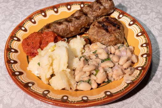 Closeup Plate With Traditional Bulgarian Food. Mashed Potato, White Beans, Haricot, Vegetable Relish Ljutenica, Grilled Minced Meat With Spices Kebapche. Horizontal Plane. High Quality Photo