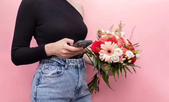 Young Caucasian Woman In Denim Holds Phone With Bouquet Of Fresh Flowers Roses, Gerbera, Chrysanthemum On Pink Background. Online Order And Flower Delivery Concept. Horizontal Plane.