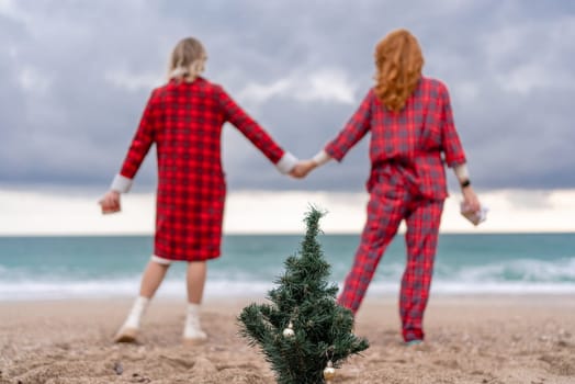 Sea two Lady in plaid shirt with a christmas tree in her hands enjoys beach. Coastal area. Christmas, New Year holidays concep.