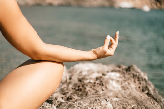 Yoga on the beach. A happy woman meditating in a yoga pose on the beach, surrounded by the ocean and rock mountains, promoting a healthy lifestyle outdoors in nature, and inspiring fitness concept