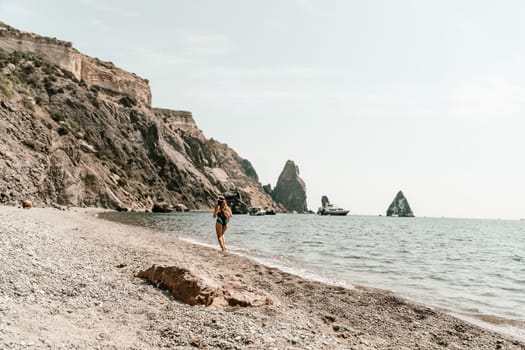 Woman beach vacation photo. A happy tourist in a blue bikini enjoying the scenic view of the sea and volcanic mountains while taking pictures to capture the memories of her travel adventure