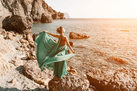 Woman green dress sea. Woman in a long mint dress posing on a beach with rocks on sunny day. Girl on the nature on blue sky background