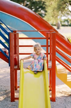 Little girl sits on top of a slide on the playground holding on to the railings. High quality photo