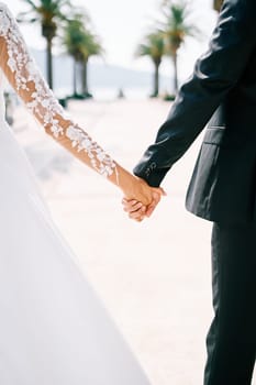 Bride and groom walk holding hands along the promenade. Cropped. Faceless. Back view. High quality photo
