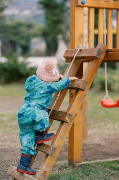 Little girl climbs a wooden ladder to a slide. Side view. High quality photo
