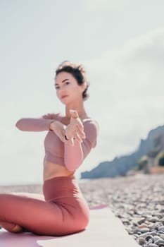 Young woman with long hair in white swimsuit and boho style braclets practicing outdoors on yoga mat by the sea on a sunset. Women's yoga fitness routine. Healthy lifestyle, harmony and meditation