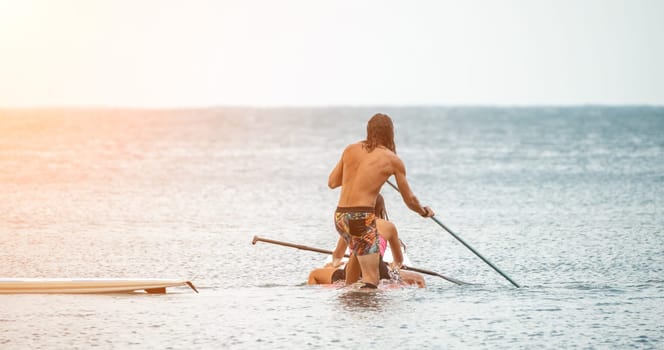 Sea woman and man on sup. Silhouette of happy young woman and man, surfing on SUP board, confident paddling through water surface. Idyllic sunset. Active lifestyle at sea or river