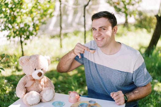 Smiling dad drinking tea from a toy cup at a table in the garden. High quality photo