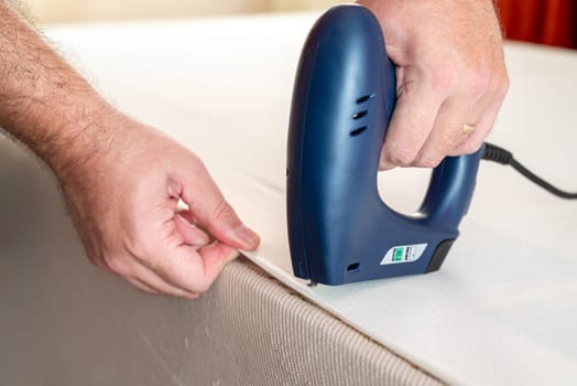 Worker stapling sofa lining with electric staple gun