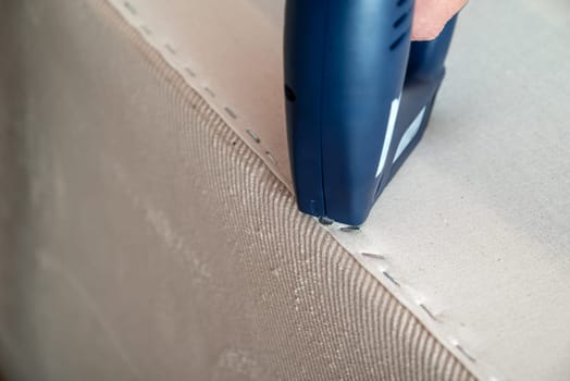 Worker stapling sofa lining with electric staple gun