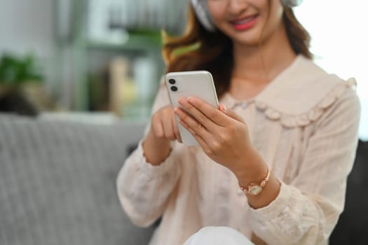 Pretty young Asian woman in headphones watching streaming tv videos online on smartphone.