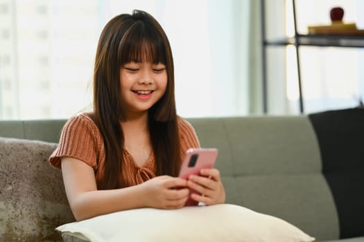 Happy asian child girl watching children content in social networks on mobile phone.