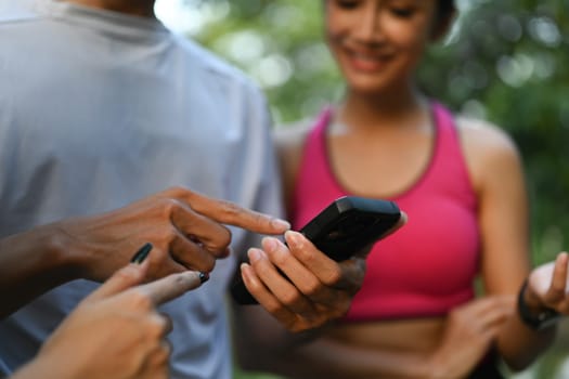 Group of sporty people checking their fitness trackers on smartphone after outdoor training