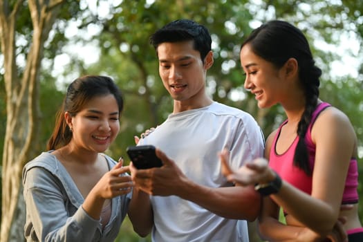 Group of sporty people checking their fitness trackers on smartphone after outdoor training