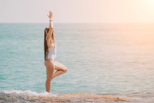 Woman sea yoga. Back view of free calm happy satisfied woman with long hair standing on top rock with yoga position against of sky by the sea. Healthy lifestyle outdoors in nature, fitness concept.