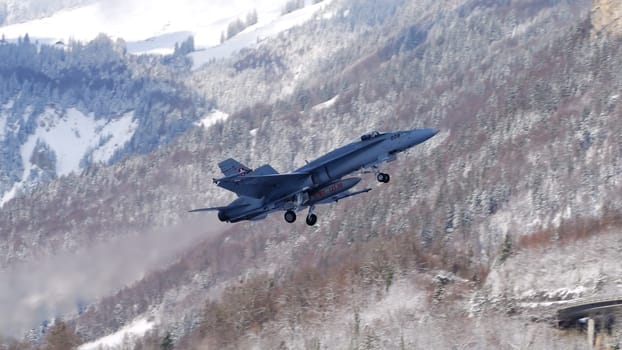 Meiringen Switzerland January 19 2023: Armed fighter jet taking off with white snow capped mountains background. Copy Space. F-18 Hornet of Swiss Air Force for Davos World Economic Forum WEF