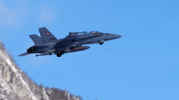 Meiringen Switzerland January 19 2023: Fighter jet retracts landing gear in blue sky at beginning of patrol mission for World Economic Forum WEF in Davos. Copy Space. F-18 Hornet of Swiss Air Force.