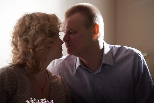 Loving adult couple communicates and embraces privately in the living room or in hotel. Woman is wearing business formal suit and man is wearing jeans and a shirt, indicating a close relationship