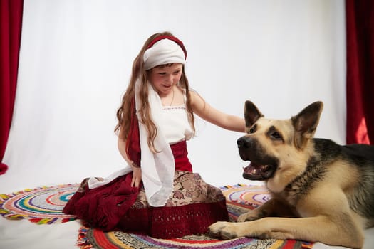 Portrait of Little girl in a stylized Tatar national costume with big shepherd dog on a white background in the studio. Photo shoot of funny young teenager who is not a professional model