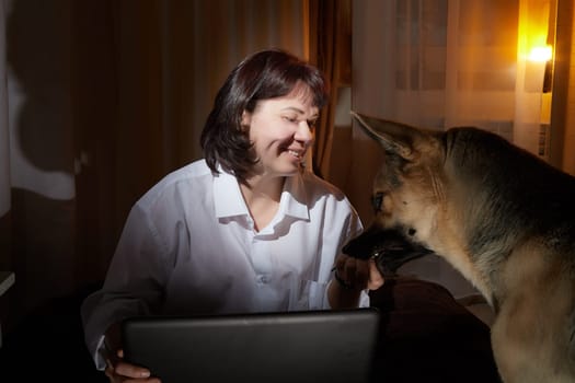 A girl in white shirt with a laptop in a dark room. A middle-aged woman works online remotely in the evening. The student is preparing for the exam at night. Blogger or freelancer in the chat