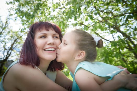 Happy mother and daughter enjoying rest, playing and fun on nature on a green lawn and with blooming apple tree in the background. Woman and girl resting outdoors in summer and spring day