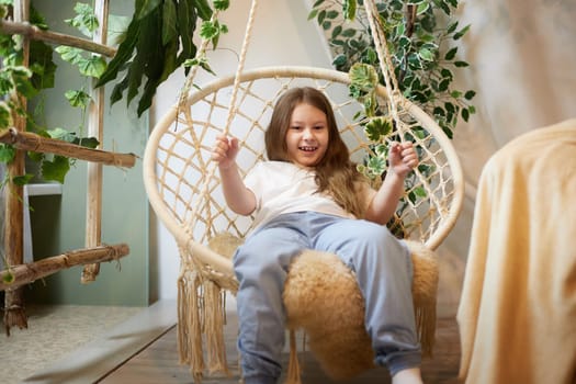 A little girl is relaxing in a room with a wicker chair. A schoolgirl is lazy after school. Teen idling at home