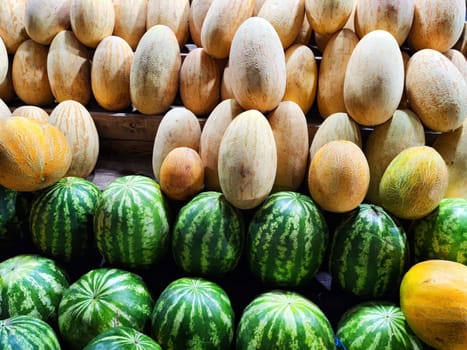 Fresh ripe green watermelons and sweet yellow melons. There are a lot of round Fruits on counter. Delicious background, texture, pattern