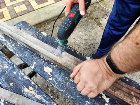 Hands of a master carpenter with an electric jigsaw in his hands cutting off piece of wood. Male hands using fret saw for cutting wood. A carpenter cuts wood with a jigsaw outdoors