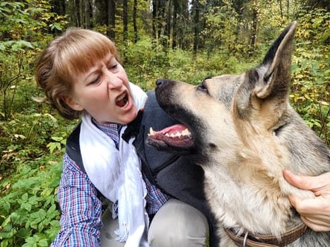 Adult girl with shepherd dog taking selfies in forest. Middle aged woman and big shepherd dog on nature. Friendship, love, communication, fun, hugs