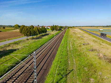 An electric railroad line with tracks next to two roads in a rural area, Germany