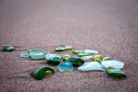 Sand beach and glass stones concept photo. Glass stones from broken bottles polished by the sea. Front view photography with blurred background. High quality picture for wallpaper, travel blog