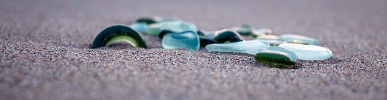Sand beach and stones with foam concept photo. Glass stones from broken bottles polished by the sea. Front view photography with blurred background. High quality picture for wallpaper, travel blog