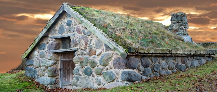 stone cabin with grass roof on sunset background