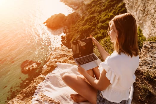 Freelance woman working on a laptop by the sea, typing away on the keyboard while enjoying the beautiful view, highlighting the idea of remote work