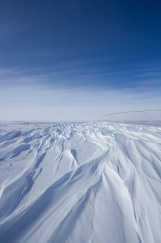 Beautiful patterns of sastrugi, parallel wavelike ridges caused by winds on surface of hard snow, with soft clouds in the sky, near Arviat Nunavut Canada